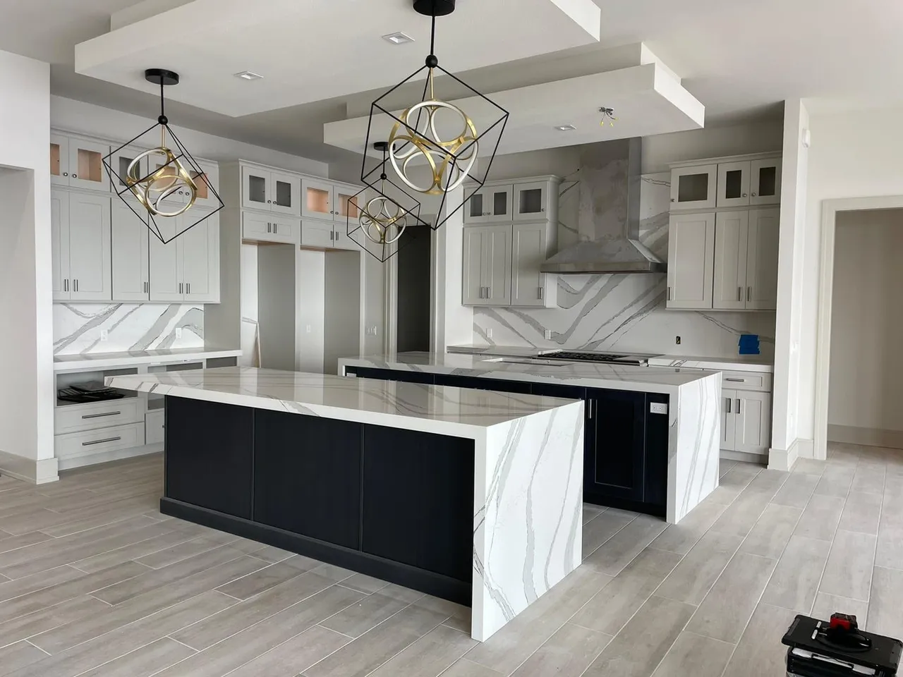 Kitchen with two black islands topped in white veined quartz with waterfall sides and a full height backsplash