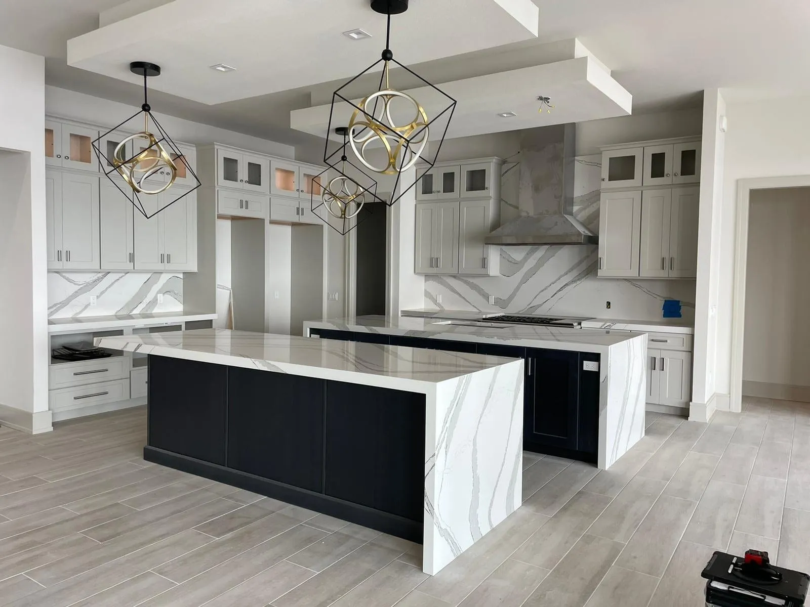 Kitchen with two navy blue islands topped in white veined quartz with waterfall sides and a full height backsplash